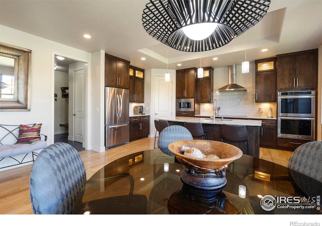 5112 Daylight Ct, Fort Collins, CO 80528 - kitchen featuring stainless steel appliances, wall chimney range hood, light wood finished floors, dark brown cabinets, and glass insert cabinets