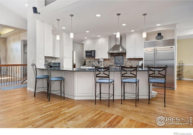 13 Blue Heron Dr, Thornton, CO 80241 - kitchen with wall chimney exhaust hood, built in appliances, dark countertops, light wood-style floors, and white cabinets