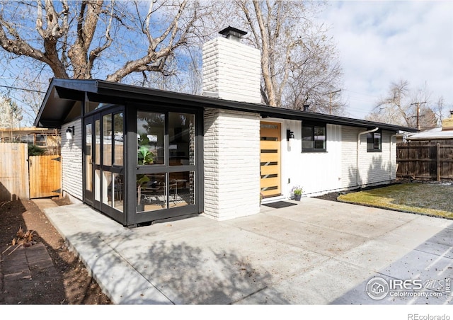 2435 S Meade St, Denver, CO 80219 - rear view of house featuring a chimney, a sunroom, a patio area, and brick siding