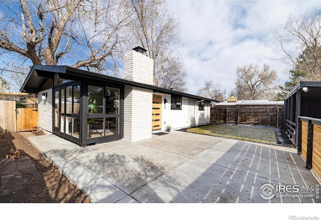 2435 S Meade St, Denver, CO 80219 - back of property featuring a sunroom, a chimney, a patio area, a fenced backyard, and brick siding