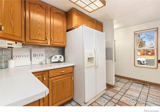 911 Timber Ct, Longmont, CO 80504 - kitchen with white refrigerator with ice dispenser, light countertops, brown cabinets, decorative backsplash, and baseboards