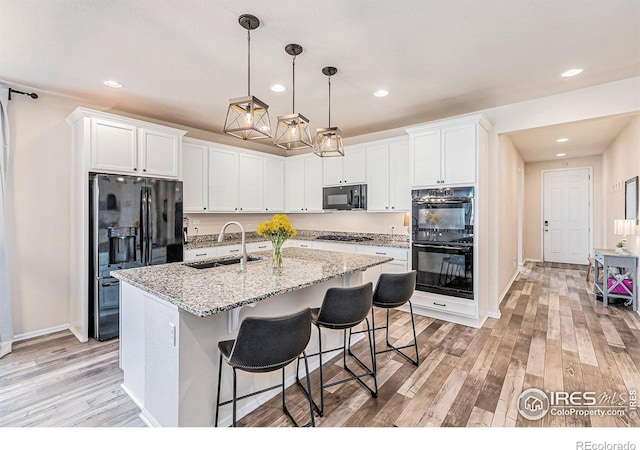 6253 Black Mesa Rd, Frederick, CO 80516 - kitchen featuring black appliances, a sink, light wood-style flooring, a kitchen island with sink, and white cabinetry