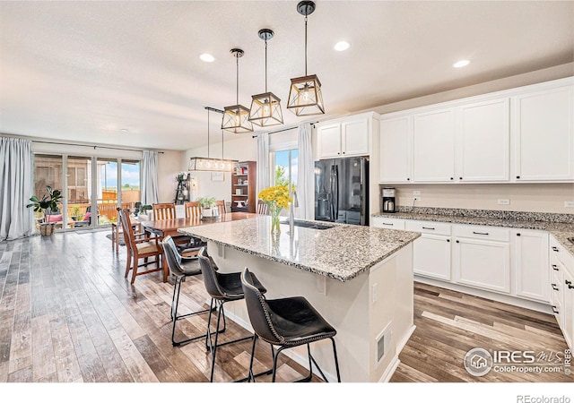 6253 Black Mesa Rd, Frederick, CO 80516 - kitchen with black fridge, a sink, light wood-type flooring, white cabinetry, and a kitchen island with sink