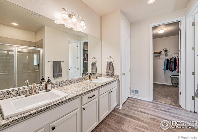 6253 Black Mesa Rd, Frederick, CO 80516 - bathroom featuring double vanity, a spacious closet, a stall shower, wood finished floors, and recessed lighting