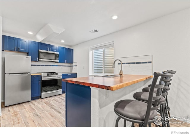 8734 19th Street Rd, Greeley, CO 80634 - kitchen featuring stainless steel appliances, wooden counters, blue cabinets, a kitchen bar, and tasteful backsplash