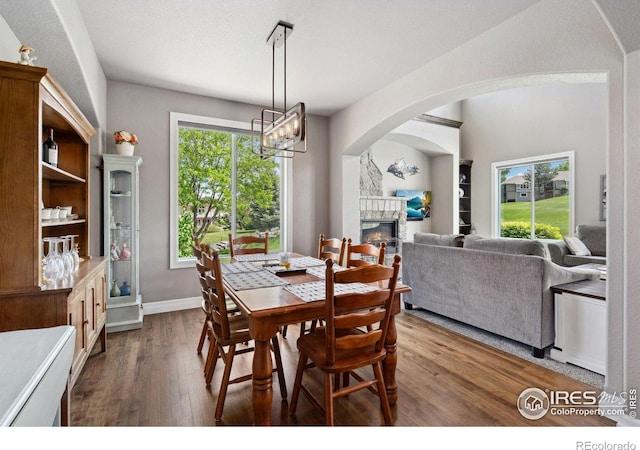 7427 Couples Ct, Fort Collins, CO 80528 - dining area with dark wood finished floors, a stone fireplace, arched walkways, a chandelier, and baseboards