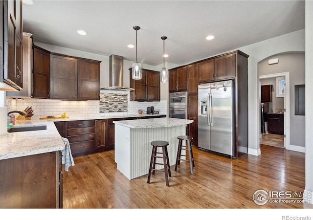 7427 Couples Ct, Fort Collins, CO 80528 - kitchen featuring stainless steel appliances, wall chimney exhaust hood, a sink, arched walkways, and dark brown cabinetry