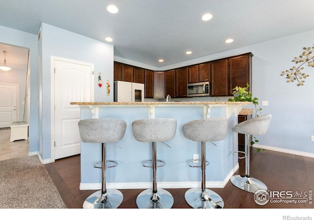 5664 Osbourne Dr, Windsor, CO 80550 - kitchen with refrigerator, stainless steel microwave, recessed lighting, dark brown cabinetry, and a kitchen bar