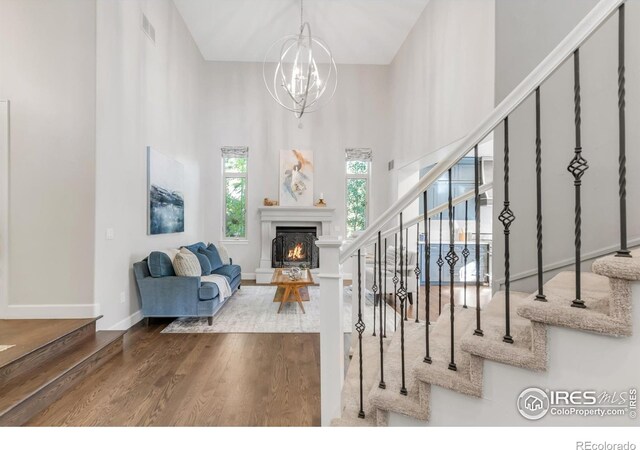 609 Corona Ct, Lafayette, CO 80026 - living room with stairs, wood finished floors, a warm lit fireplace, a chandelier, and a high ceiling