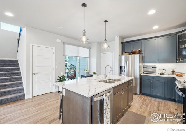 6211 Stable View St, Castle Pines, CO 80108 - kitchen with stainless steel appliances, a sink, light wood-type flooring, a center island with sink, and glass insert cabinets