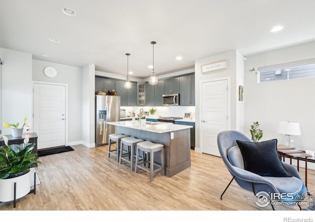 6211 Stable View St, Castle Pines, CO 80108 - kitchen with appliances with stainless steel finishes, a kitchen breakfast bar, light wood-style flooring, a kitchen island with sink, and recessed lighting