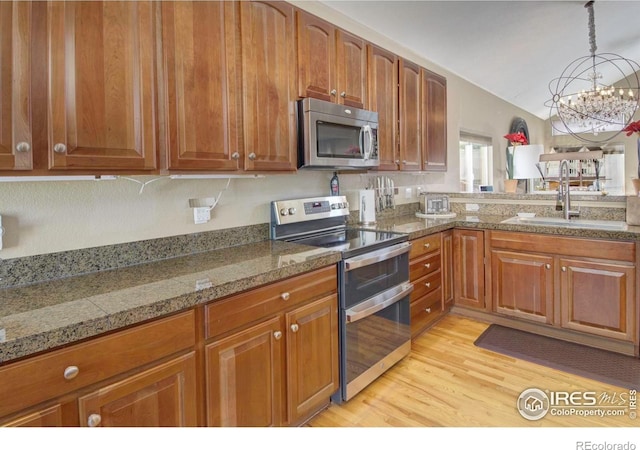 2085 Tundra Cir, Erie, CO 80516 - kitchen with appliances with stainless steel finishes, a sink, brown cabinets, light wood-style floors, and a chandelier
