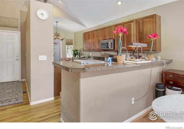 2085 Tundra Cir, Erie, CO 80516 - kitchen featuring appliances with stainless steel finishes, lofted ceiling, light wood finished floors, brown cabinetry, and light countertops