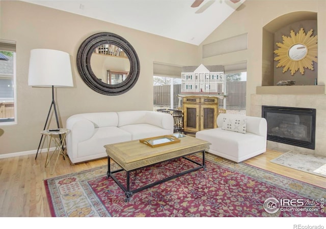 2085 Tundra Cir, Erie, CO 80516 - living room featuring wood finished floors, a tiled fireplace, ceiling fan, high vaulted ceiling, and baseboards