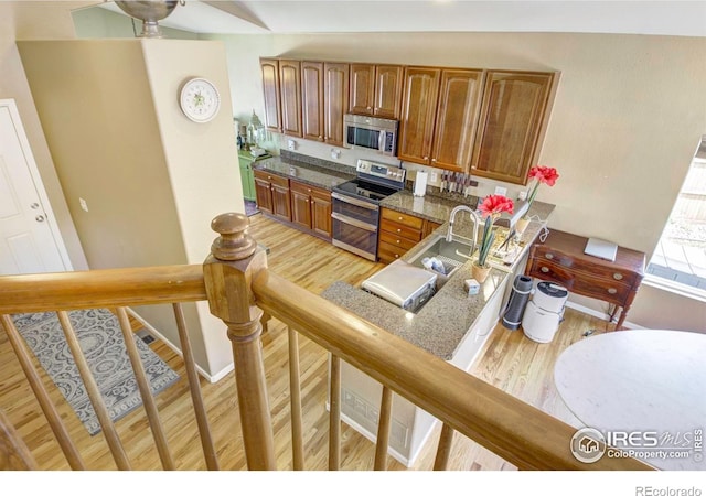 2085 Tundra Cir, Erie, CO 80516 - kitchen with appliances with stainless steel finishes, light wood finished floors, brown cabinetry, a sink, and dark stone countertops
