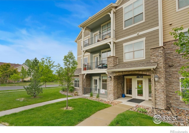 4672 Hahns Peak Dr Unit 101, Loveland, CO 80538 - view of front facade featuring a balcony, stone siding, a front yard, and french doors
