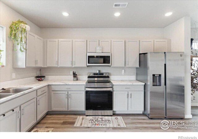 608 Apex Trl, Ault, CO 80610 - kitchen with appliances with stainless steel finishes, light wood finished floors, recessed lighting, light stone counters, and a sink
