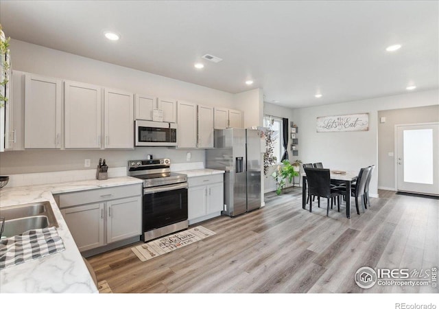 608 Apex Trl, Ault, CO 80610 - kitchen with appliances with stainless steel finishes, light wood-style floors, recessed lighting, light stone counters, and a sink