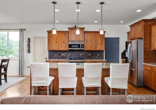 873 Signal Ct, Timnath, CO 80547 - kitchen with appliances with stainless steel finishes, brown cabinetry, decorative backsplash, recessed lighting, and light wood-style flooring