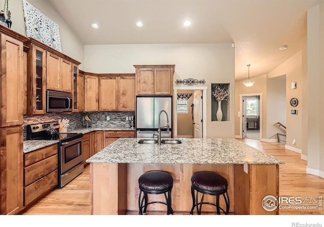 405 Timber Ridge Parkway, Severance, CO 80550 - kitchen featuring appliances with stainless steel finishes, a sink, a kitchen breakfast bar, tasteful backsplash, and light wood-style flooring