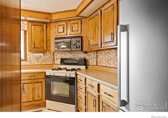 1155 Caroline Ct, Loveland, CO 80537 - kitchen with white gas stove, fridge, stainless steel microwave, light countertops, and brown cabinets