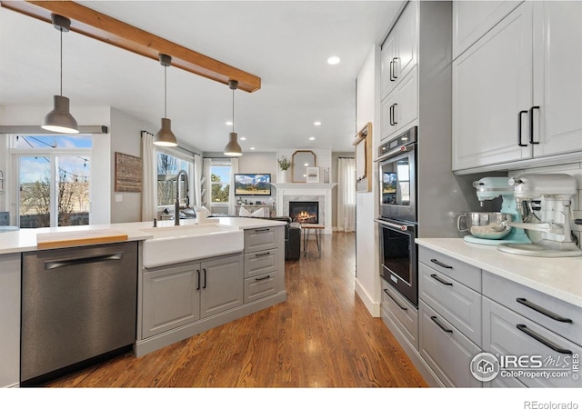 6434 Cloudburst Ave, Timnath, CO 80547 - kitchen featuring stainless steel appliances, a sink, gray cabinets, dark wood finished floors, and a glass covered fireplace