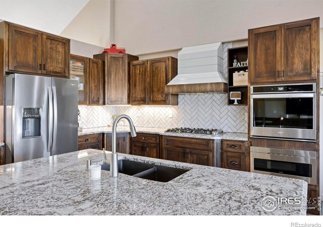 33820 County Road 47, Greeley, CO 80631 - kitchen featuring stainless steel appliances, wall chimney range hood, a sink, decorative backsplash, and light stone countertops