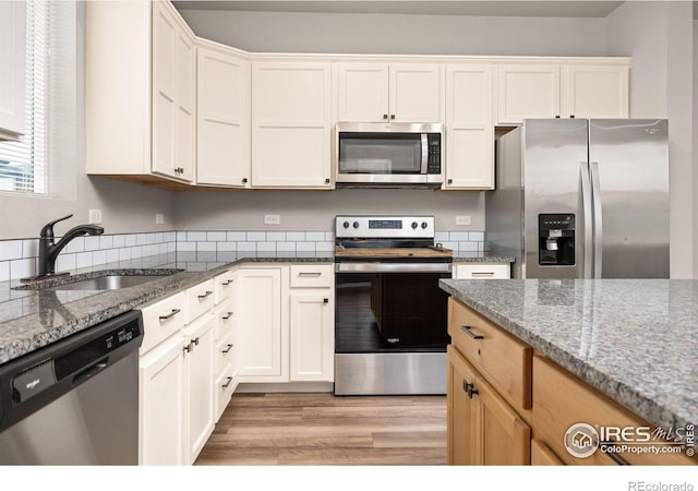 3925 Buckthorn St, Wellington, CO 80549 - kitchen with stainless steel appliances, a sink, stone counters, light wood-style floors, and white cabinets