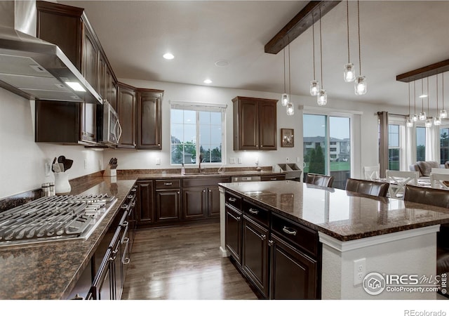 6356 Twilight Ave, Firestone, CO 80504 - kitchen featuring wall chimney exhaust hood, appliances with stainless steel finishes, a center island, dark wood-type flooring, and dark stone countertops