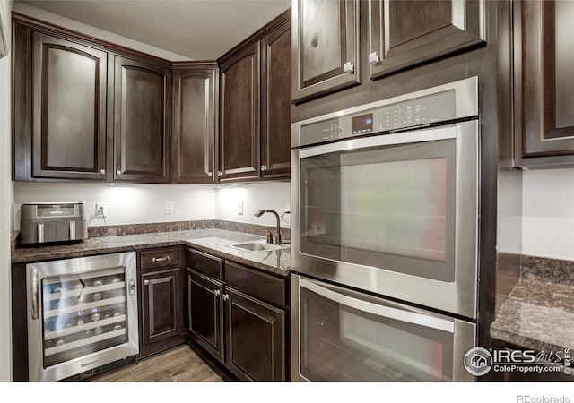 6356 Twilight Ave, Firestone, CO 80504 - kitchen featuring beverage cooler, stainless steel double oven, a sink, dark brown cabinets, and dark stone countertops