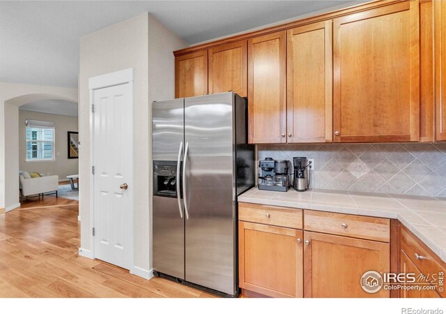 13255 Red Deer Trl, Broomfield, CO 80020 - kitchen featuring stainless steel fridge, arched walkways, tile countertops, tasteful backsplash, and light wood-style floors