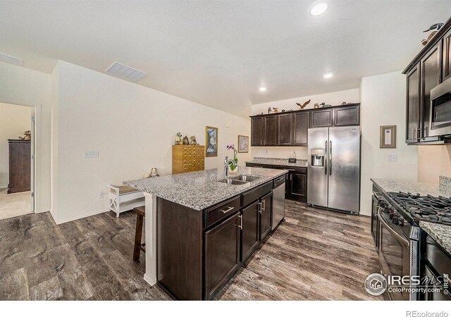 926 Birchdale Ct, Windsor, CO 80550 - kitchen with appliances with stainless steel finishes, a sink, dark wood finished floors, light stone countertops, and a kitchen island with sink