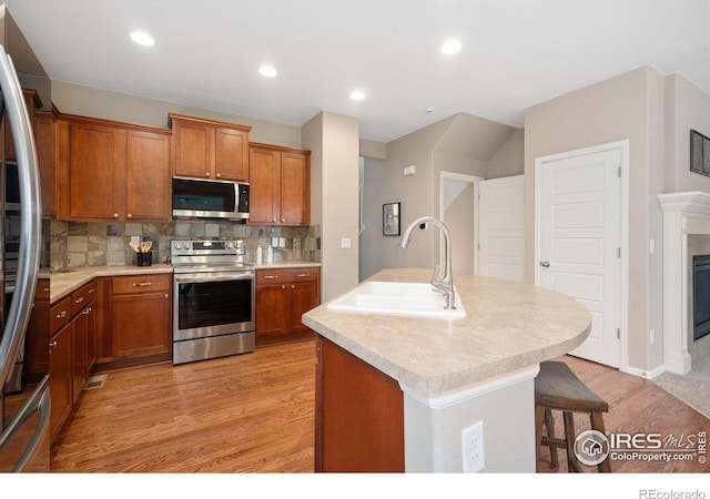 6492 Richland Ave, Timnath, CO 80547 - kitchen with appliances with stainless steel finishes, a sink, light wood-style flooring, brown cabinets, and a breakfast bar area