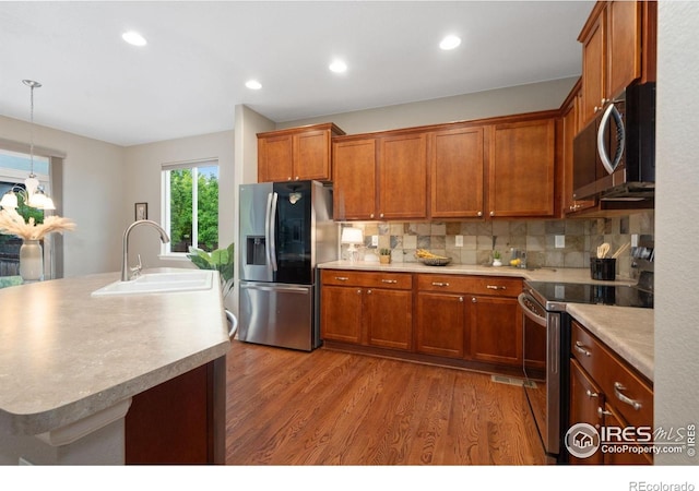 6492 Richland Ave, Timnath, CO 80547 - kitchen with stainless steel appliances, a sink, wood finished floors, brown cabinets, and decorative backsplash