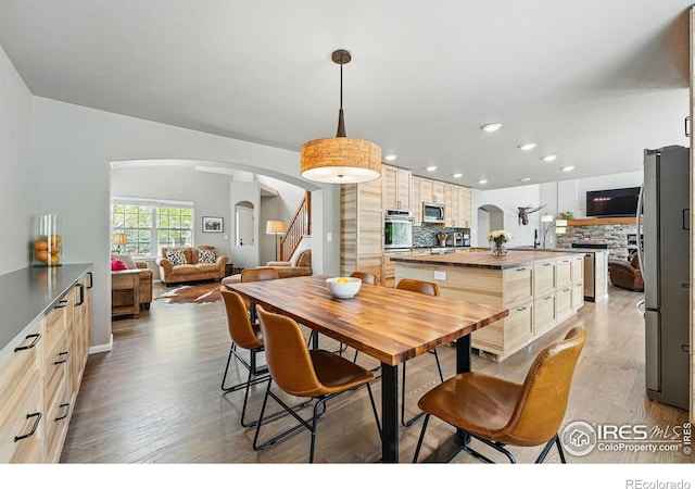 682 Briar Dale Dr, Castle Pines, CO 80108 - dining area featuring arched walkways, light wood-style floors, recessed lighting, a fireplace, and stairs