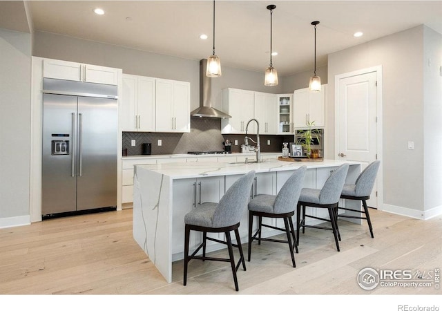 730 Promenade Dr, Superior, CO 80027 - kitchen with stainless steel built in fridge, wall chimney exhaust hood, light wood-style flooring, tasteful backsplash, and white cabinetry