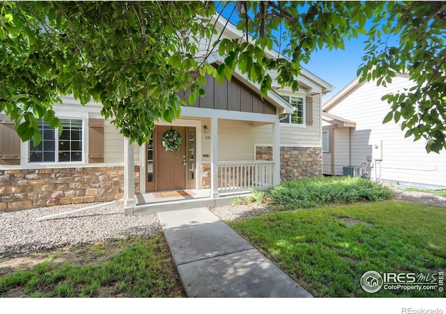 1974 E 11th St, Loveland, CO 80537 - entrance to property featuring stone siding, a porch, cooling unit, and board and batten siding