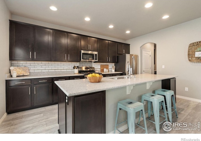 426 Gannet Peak Dr, Windsor, CO 80550 - kitchen with stainless steel appliances, light wood finished floors, a sink, arched walkways, and a breakfast bar