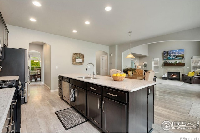 426 Gannet Peak Dr, Windsor, CO 80550 - kitchen with a sink, arched walkways, black gas range oven, light wood-style floors, and a glass covered fireplace