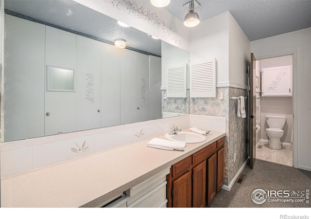 2409 Flora Dr, Loveland, CO 80537 - bathroom with vanity, toilet, a textured ceiling, and a wainscoted wall