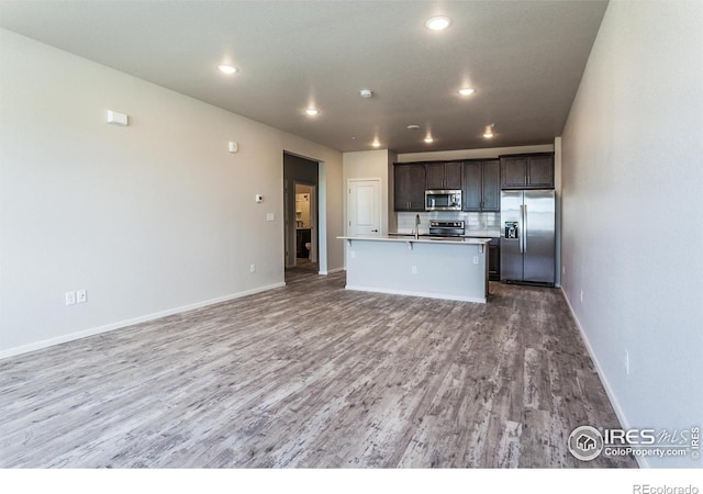 1811 Bounty Dr Unit 4, Windsor, CO 80550 - kitchen with stainless steel appliances, wood finished floors, open floor plan, a kitchen island with sink, and dark brown cabinetry