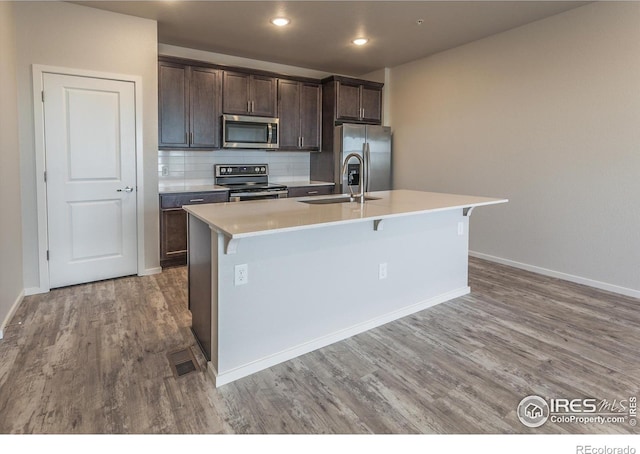 1811 Bounty Dr Unit 4, Windsor, CO 80550 - kitchen with appliances with stainless steel finishes, a kitchen island with sink, wood finished floors, dark brown cabinetry, and light countertops