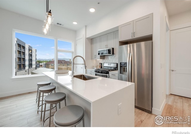 2876 W 53rd Ave Unit 301, Denver, CO 80221 - kitchen with stainless steel appliances, a sink, light wood finished floors, a breakfast bar, and a center island with sink