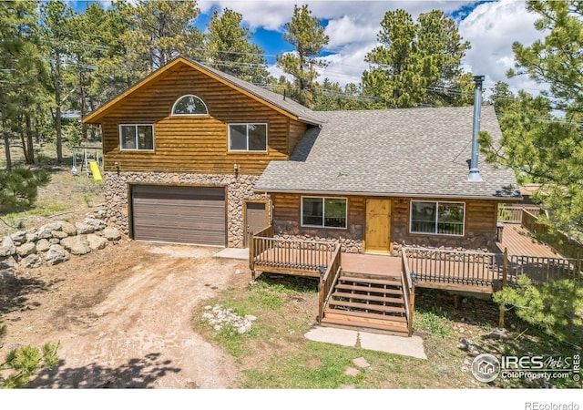 24192 W County Road 74e, Red Feather Lakes, CO 80545 - view of front of property with a wooden deck, stone siding, dirt driveway, an attached garage, and roof with shingles
