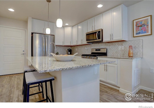 5863 Boston St, Denver, CO 80238 - kitchen featuring stainless steel appliances, light wood finished floors, white cabinetry, backsplash, and light stone counters