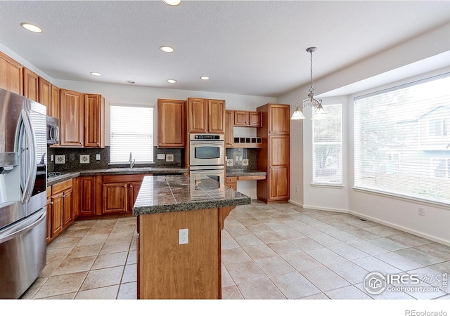 2631 E 136th Pl, Thornton, CO 80602 - kitchen featuring tile counters, appliances with stainless steel finishes, a kitchen island, tasteful backsplash, and a sink
