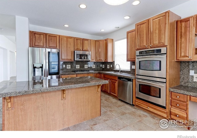 2631 E 136th Pl, Thornton, CO 80602 - kitchen featuring appliances with stainless steel finishes, tile countertops, a sink, a kitchen breakfast bar, and decorative backsplash