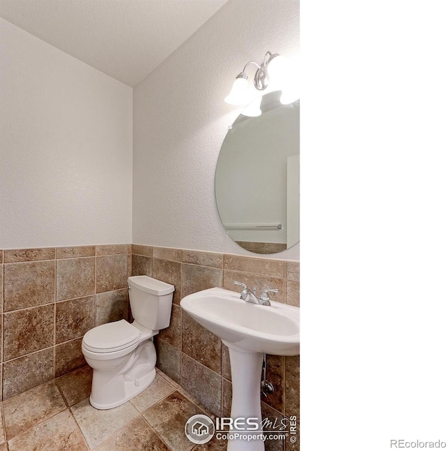2631 E 136th Pl, Thornton, CO 80602 - half bathroom featuring toilet, tile walls, and a sink
