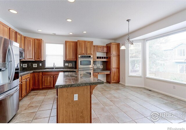 2631 E 136th Pl, Thornton, CO 80602 - kitchen featuring stainless steel appliances, tile countertops, a center island, tasteful backsplash, and a kitchen bar