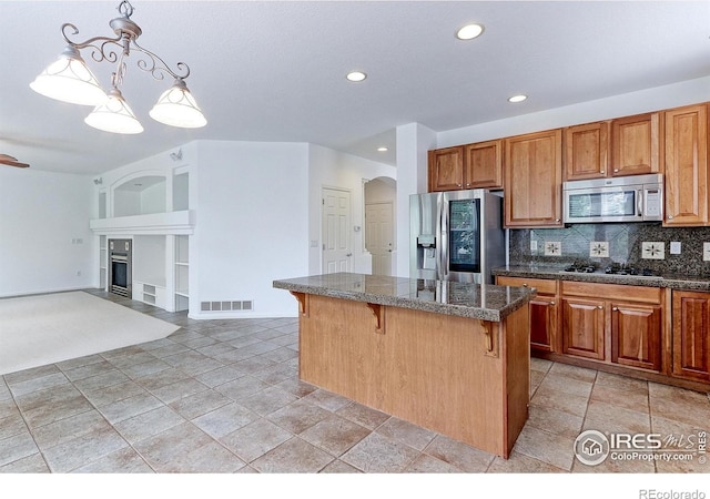 2631 E 136th Pl, Thornton, CO 80602 - kitchen with appliances with stainless steel finishes, a kitchen bar, a fireplace with flush hearth, a center island, and tasteful backsplash